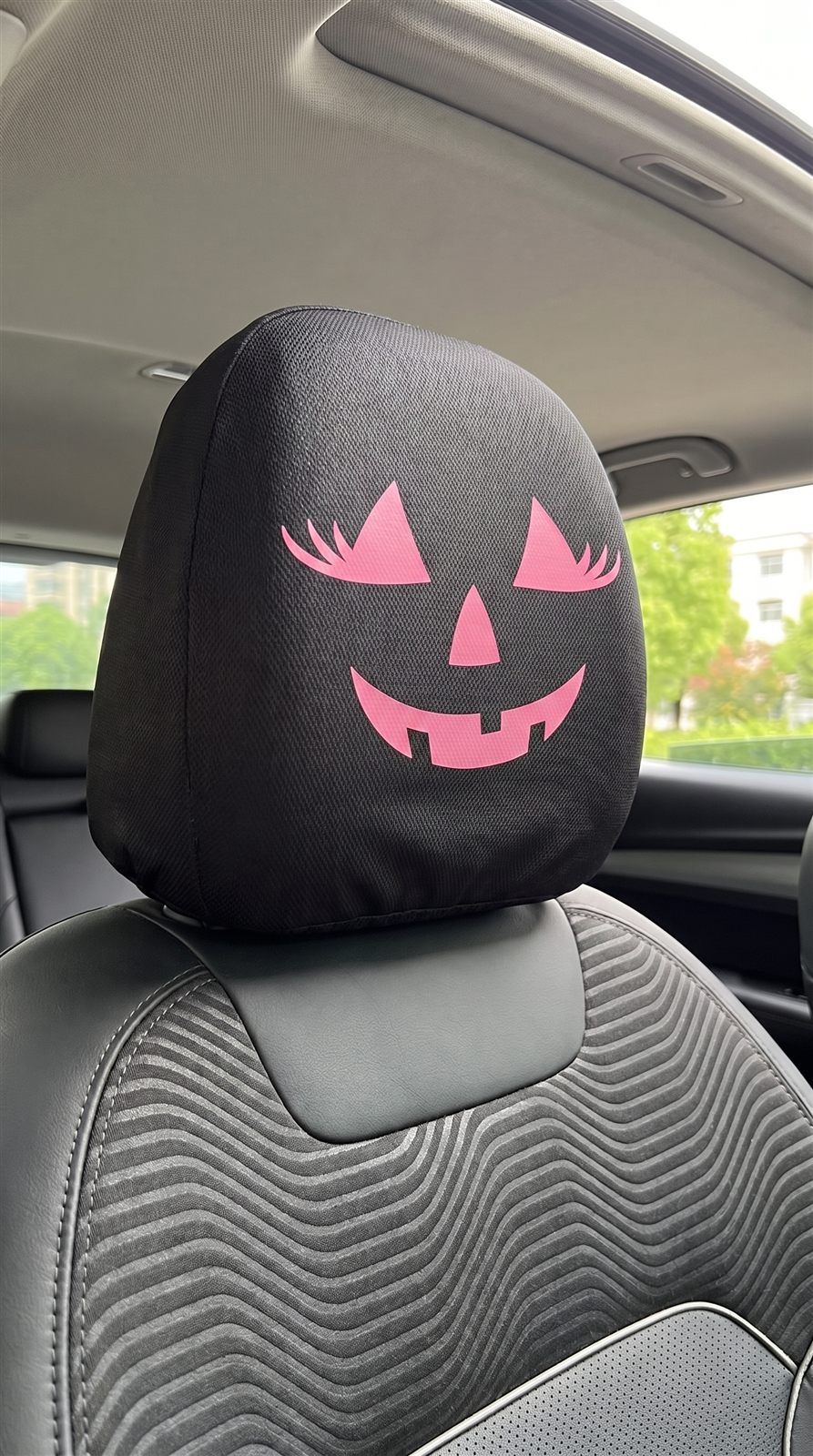 Pink jack-o-lantern face on a black car headrest cover